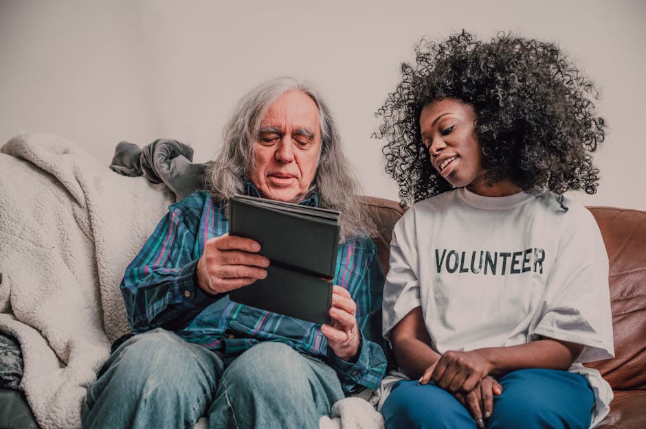 Young volunteer helps senior man with technology, fostering connection indoors.